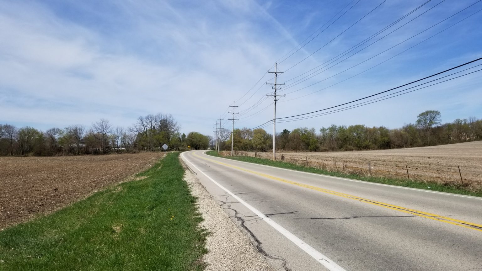 Rural curved road with farmland on both sides and utility poles